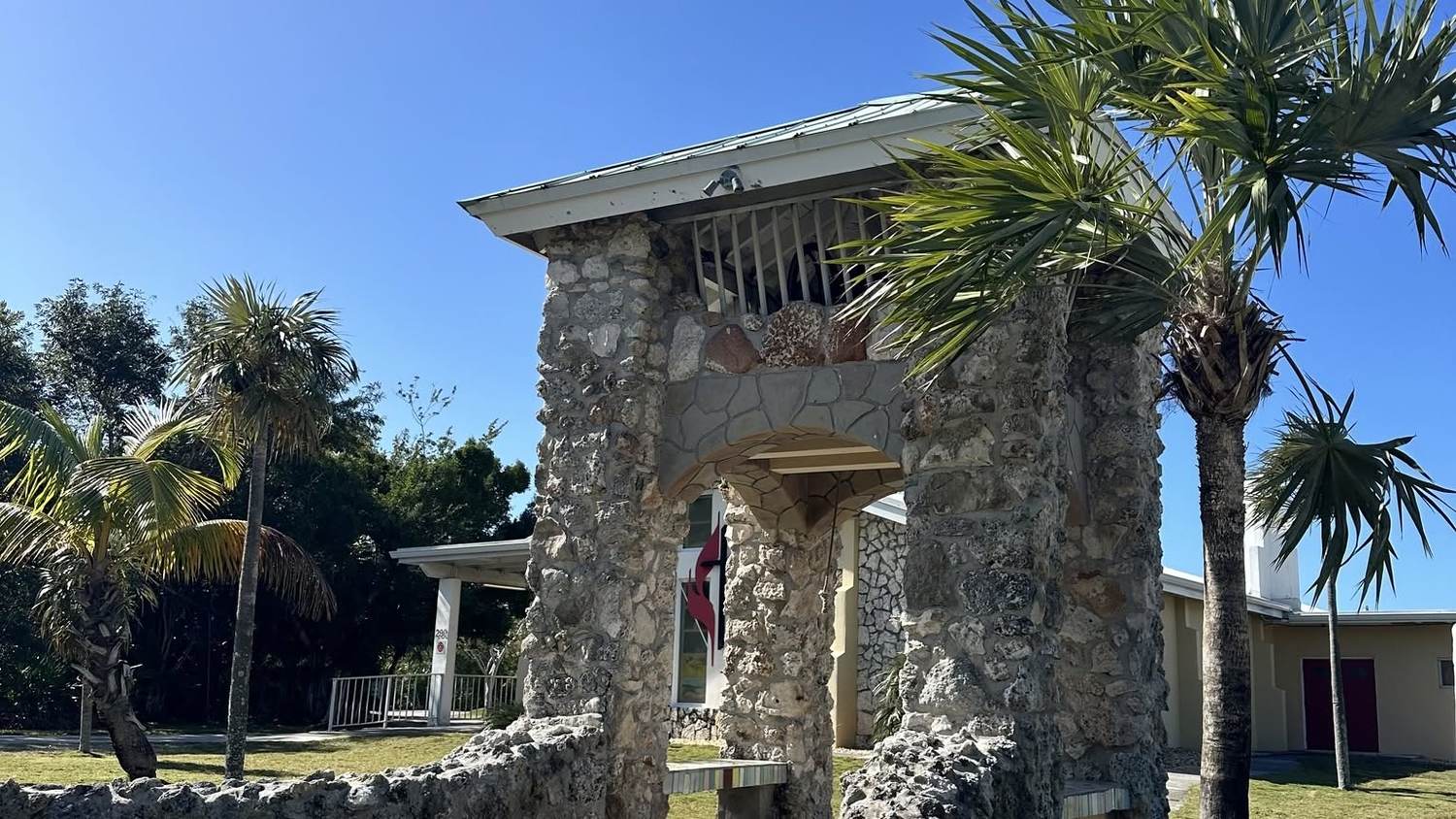 The coral-rock bell tower at the entrance of Big Pine United Methodist Church, framed by palm trees under a clear blue sky