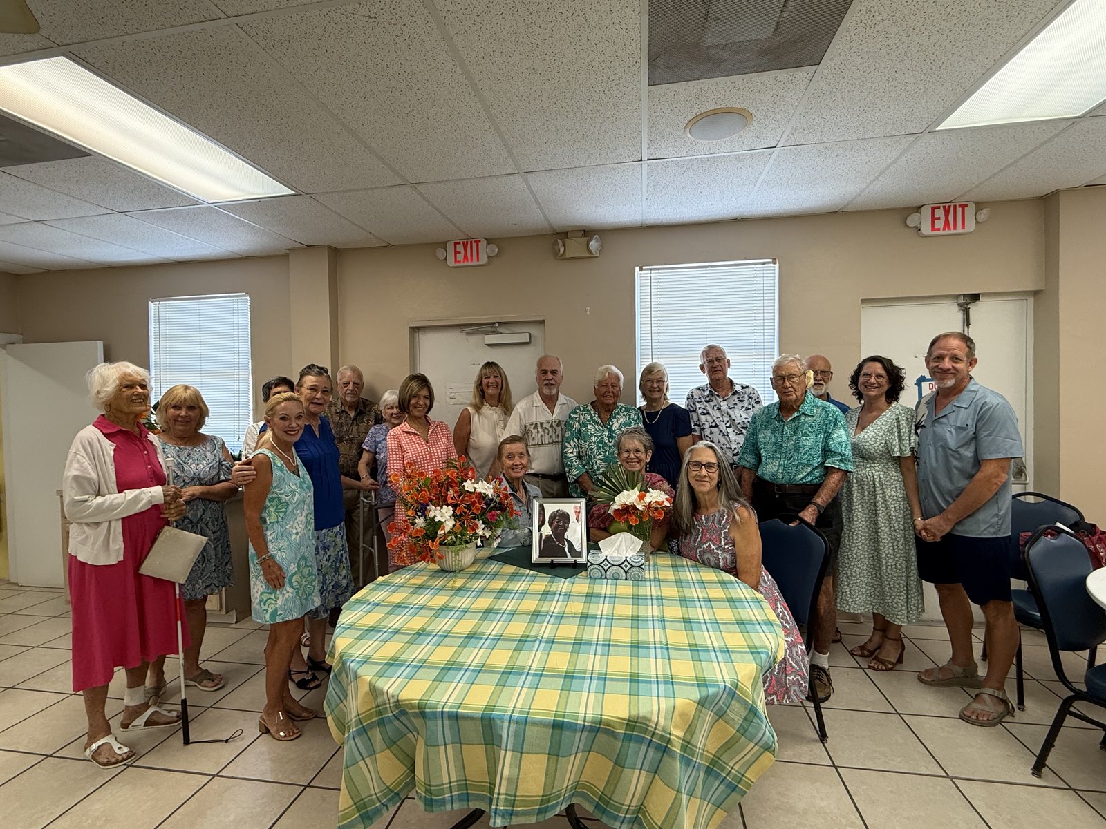 About two dozen members of the congregation gathered together around a table with flowers in the Social Hall